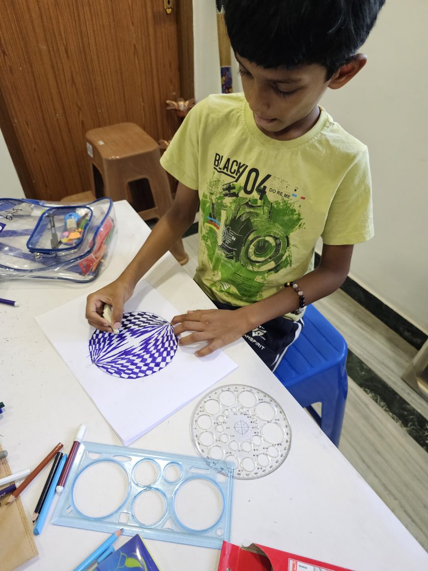 A young student carefully drawing a blue mandala with a circle template and coloured pens