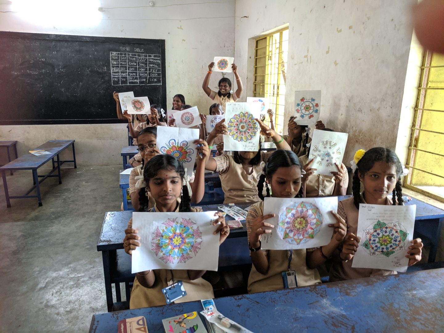School girls in a Chennai classroom proudly holding up the mandalas they drew in a Varaaz Arts workshop