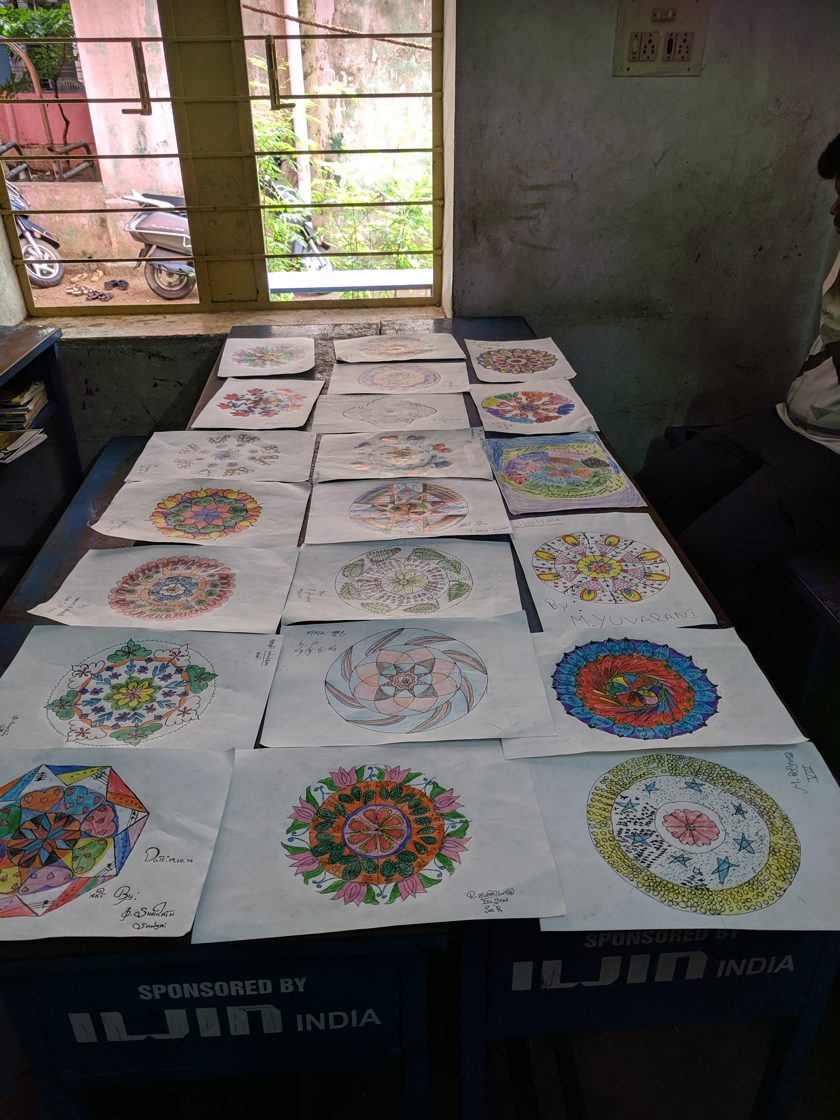 A long table covered with colourful mandalas drawn by school students, laid out like an exhibition